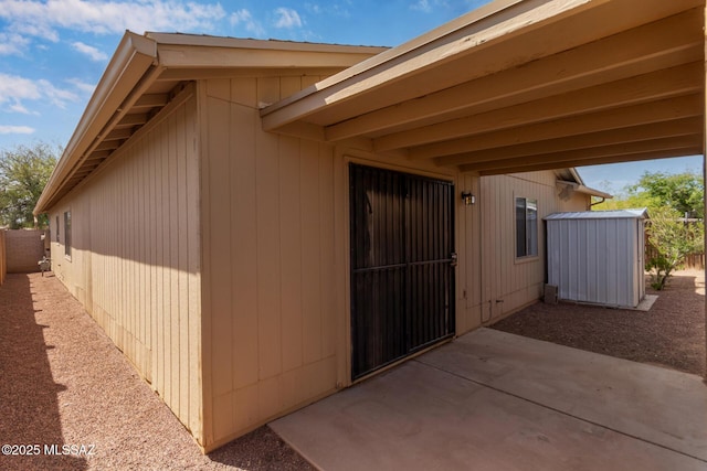 view of side of property with a patio, a storage unit, fence, and an outbuilding