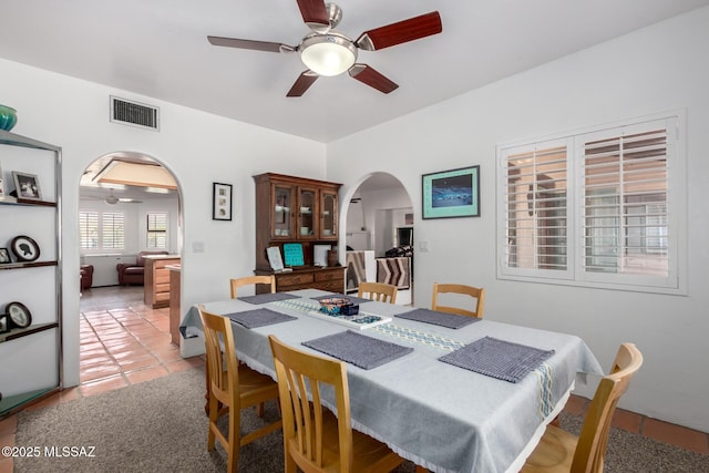 dining room featuring arched walkways, visible vents, a ceiling fan, and light tile patterned flooring