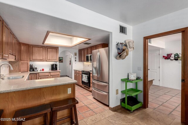 kitchen featuring a peninsula, light countertops, stainless steel appliances, arched walkways, and a sink