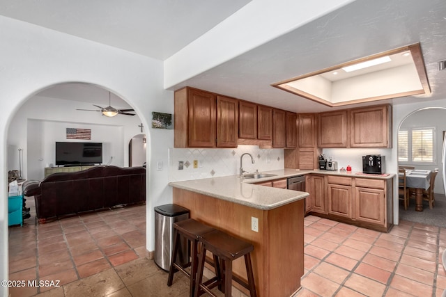 kitchen with arched walkways, a peninsula, a sink, a raised ceiling, and decorative backsplash