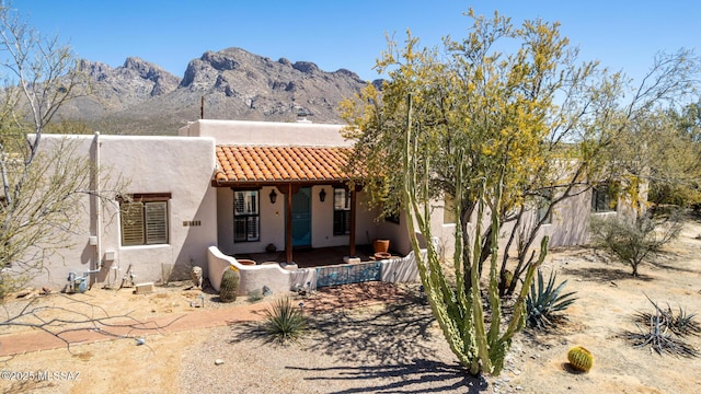 rear view of property with a porch, stucco siding, a tiled roof, and a mountain view