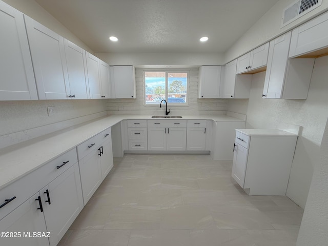 kitchen with white cabinets, visible vents, recessed lighting, a sink, and backsplash