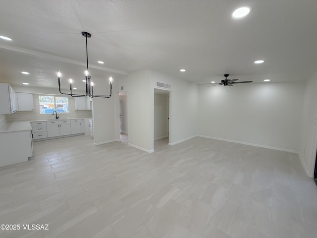 unfurnished living room featuring baseboards, recessed lighting, visible vents, ceiling fan with notable chandelier, and a sink