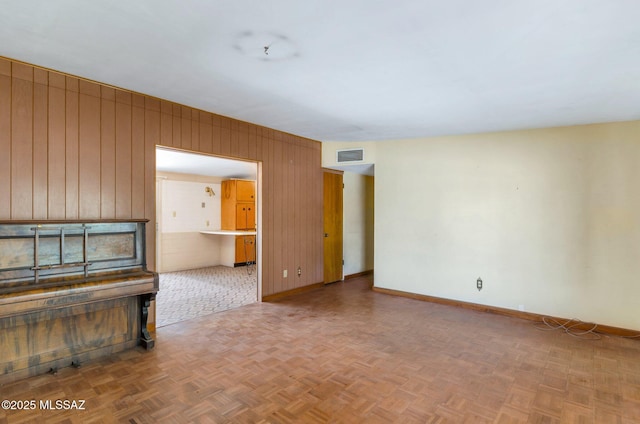 unfurnished living room featuring wooden walls, visible vents, and baseboards