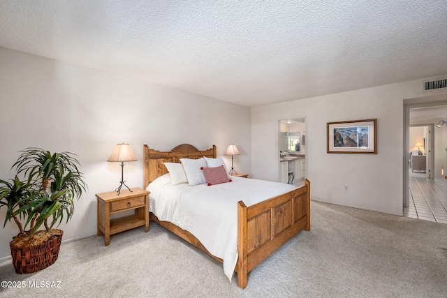 bedroom featuring a textured ceiling, light colored carpet, ensuite bathroom, and visible vents