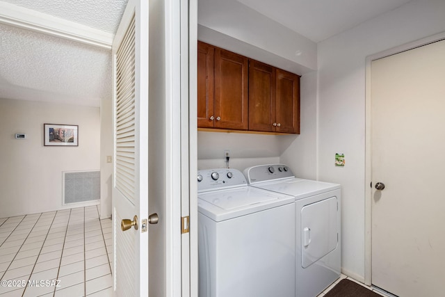 clothes washing area with light tile patterned floors, a textured ceiling, visible vents, washing machine and dryer, and cabinet space
