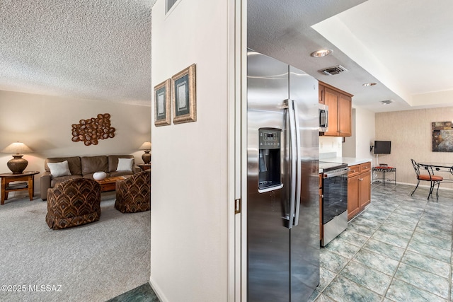 kitchen featuring visible vents, open floor plan, a textured ceiling, brown cabinetry, and stainless steel appliances