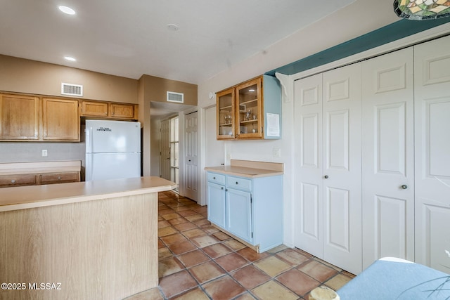 kitchen with visible vents, light countertops, freestanding refrigerator, and glass insert cabinets