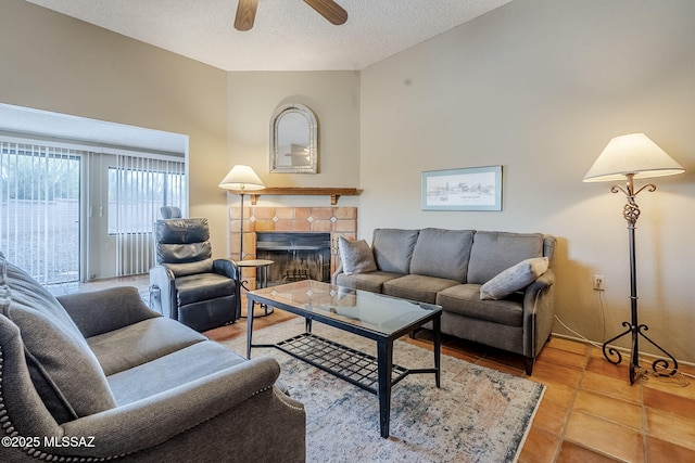 living room featuring ceiling fan, a textured ceiling, tile patterned flooring, and a fireplace