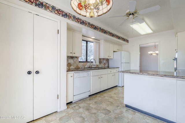 kitchen featuring dark stone countertops, a sink, ceiling fan with notable chandelier, white appliances, and backsplash
