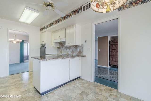 kitchen featuring white cabinetry, visible vents, oven, ceiling fan with notable chandelier, and backsplash