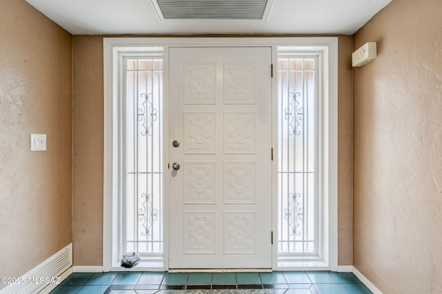 tiled entryway with visible vents, a textured wall, and baseboards