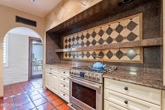 4401 E Havasu Rd, Tucson, AZ 85718 - kitchen featuring dark stone countertops, visible vents, arched walkways, gas range, and backsplash
