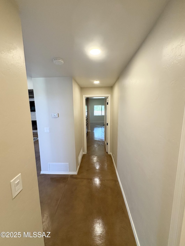 hall with visible vents, baseboards, and finished concrete floors