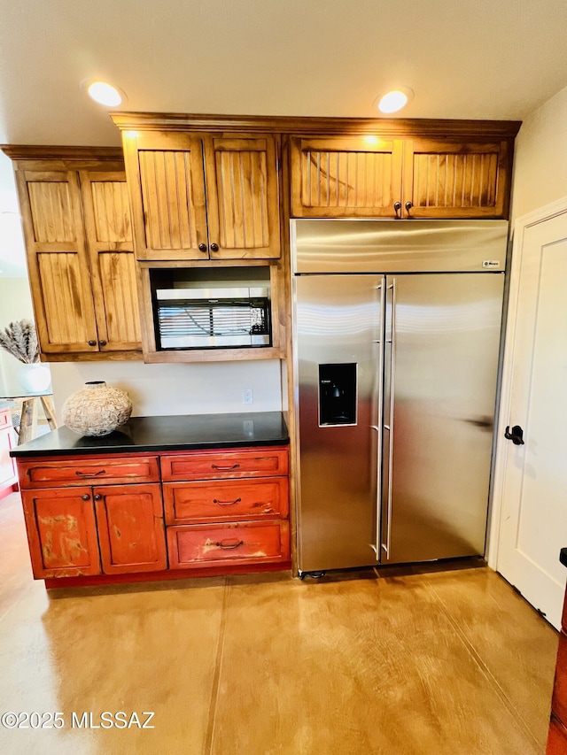 kitchen with dark countertops, stainless steel built in refrigerator, and concrete floors