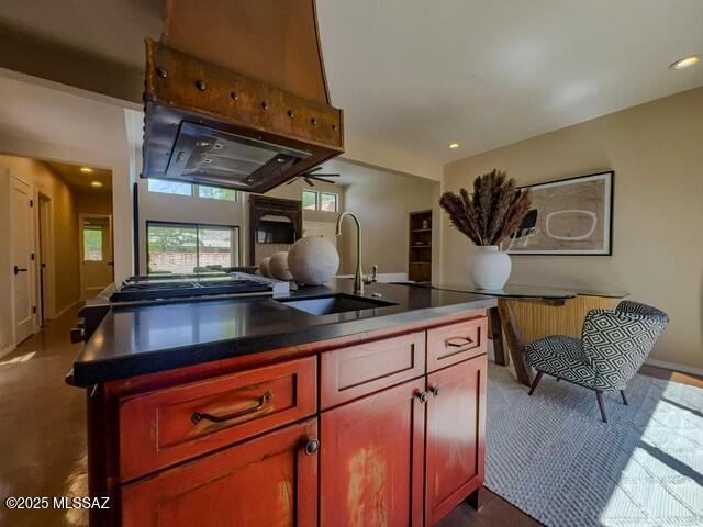 kitchen featuring a kitchen island with sink, a sink, dark brown cabinets, dark countertops, and recessed lighting