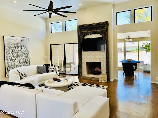 living area featuring a ceiling fan, a high ceiling, a fireplace, and concrete floors