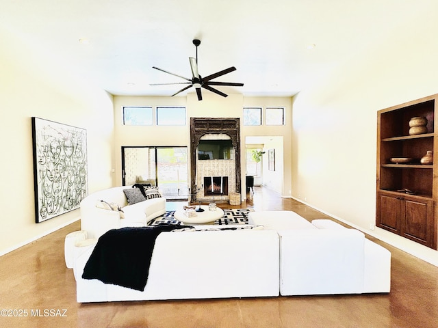 living area with a fireplace with raised hearth, a towering ceiling, baseboards, and ceiling fan