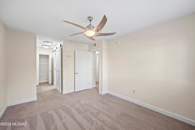 unfurnished bedroom with a ceiling fan, visible vents, a barn door, carpet flooring, and baseboards