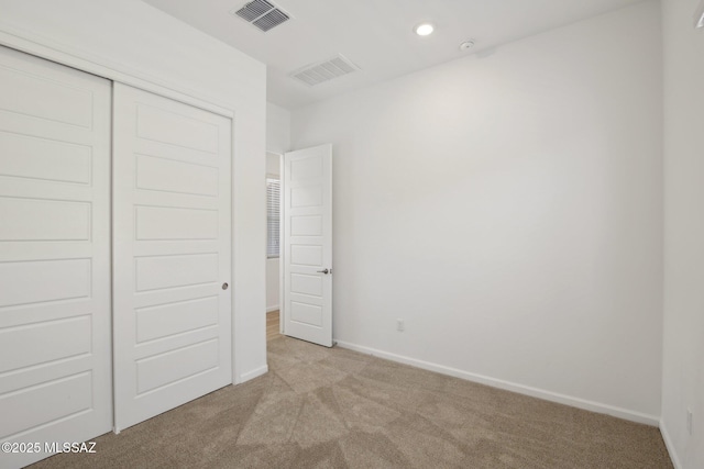 unfurnished bedroom featuring visible vents, baseboards, a closet, and light carpet