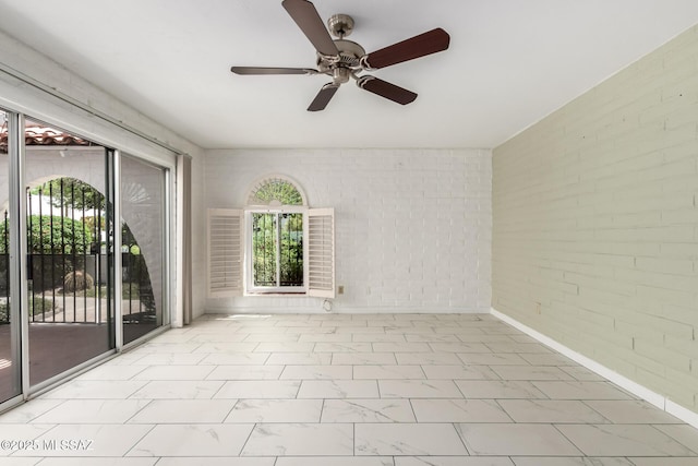 spare room with ceiling fan, a healthy amount of sunlight, marble finish floor, and brick wall