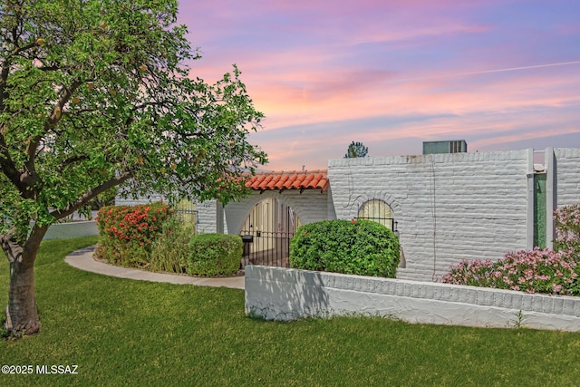 view of front of house featuring fence, a tiled roof, and a front lawn