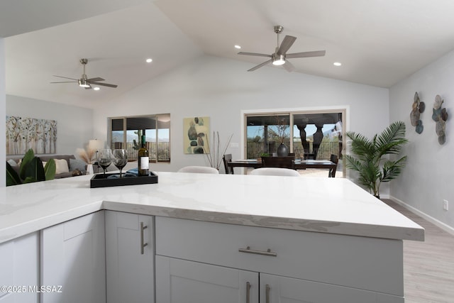 kitchen with ceiling fan, light stone counters, lofted ceiling, light wood-style flooring, and open floor plan