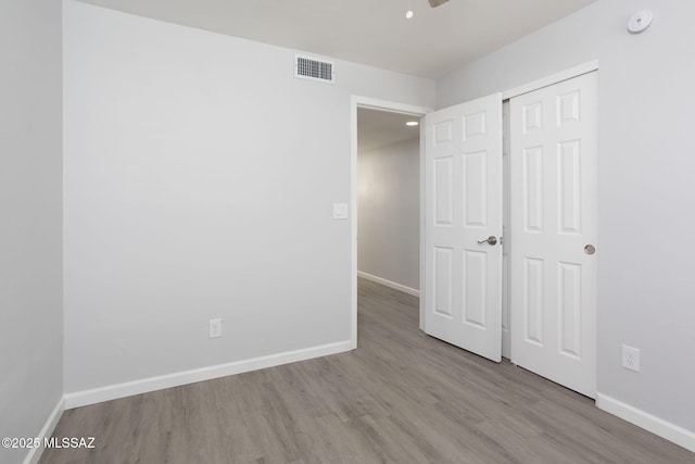 unfurnished bedroom with baseboards, visible vents, wood finished floors, and a closet