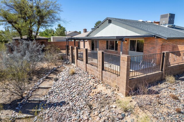 exterior space featuring fence, central air condition unit, roof with shingles, and brick siding