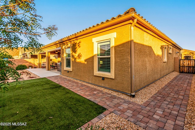 back of property with a patio area, stucco siding, fence, and a yard