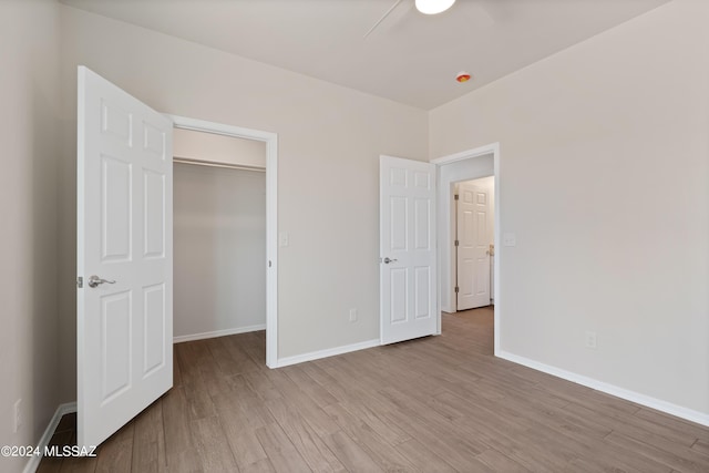 unfurnished bedroom featuring a spacious closet, light wood finished floors, and baseboards