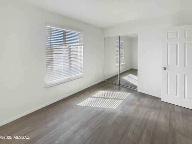 unfurnished bedroom with wood finished floors, baseboards, and a closet