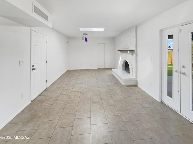 unfurnished living room featuring visible vents, light tile patterned floors, a skylight, and a brick fireplace