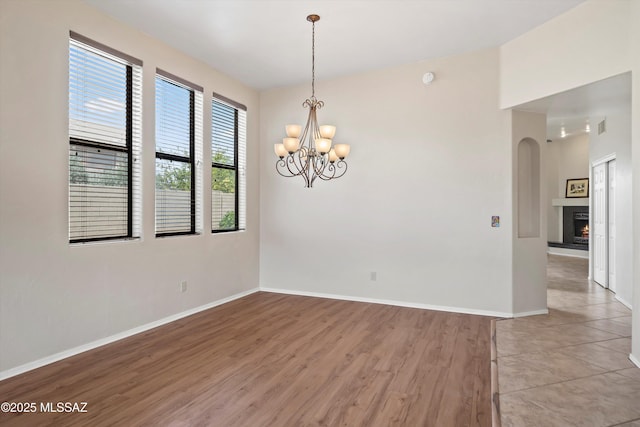 11460 N Palmetto Dunes Ave, Tucson, AZ 85737 - spare room featuring a chandelier, light wood-style floors, baseboards, and a warm lit fireplace