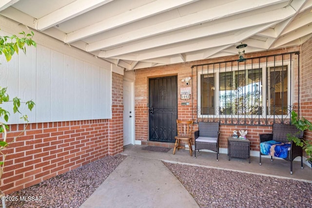 view of exterior entry featuring a porch and brick siding