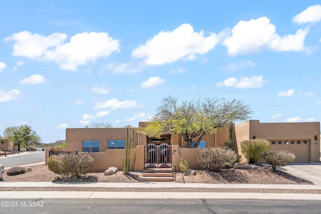 pueblo revival-style home featuring a fenced front yard, stucco siding, concrete driveway, and a garage
