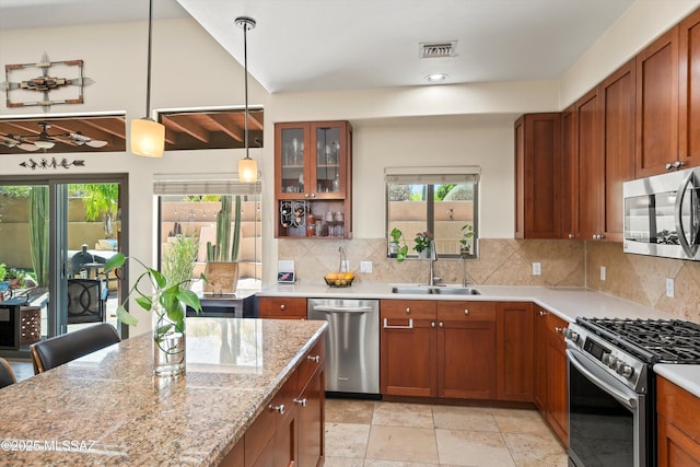kitchen featuring glass insert cabinets, backsplash, brown cabinets, appliances with stainless steel finishes, and a sink