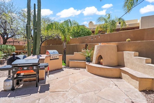 view of patio / terrace with a grill, fence, and a lit fireplace
