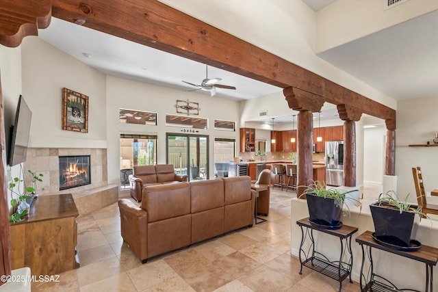 living room featuring visible vents, a ceiling fan, beamed ceiling, a towering ceiling, and a tile fireplace