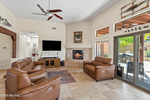 living area with a tile fireplace, visible vents, and a ceiling fan