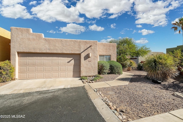 adobe home with an attached garage, aphalt driveway, and stucco siding