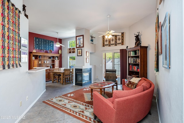 tiled living room with ceiling fan, baseboards, and a multi sided fireplace