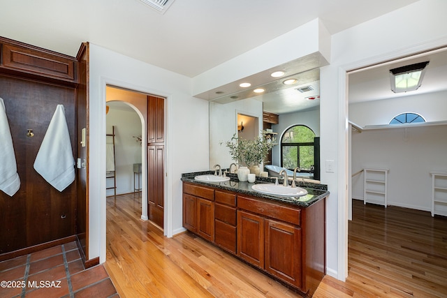full bathroom with a sink, visible vents, double vanity, and wood finished floors