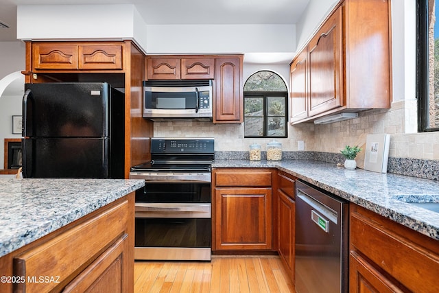 kitchen featuring tasteful backsplash, brown cabinetry, appliances with stainless steel finishes, and light wood-style floors