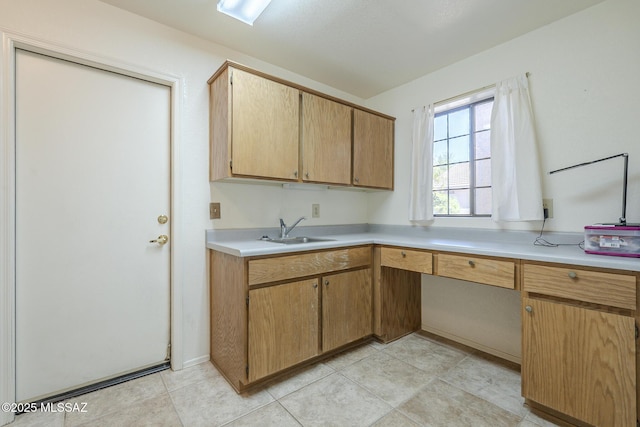 kitchen with light countertops, built in desk, a sink, and light tile patterned flooring