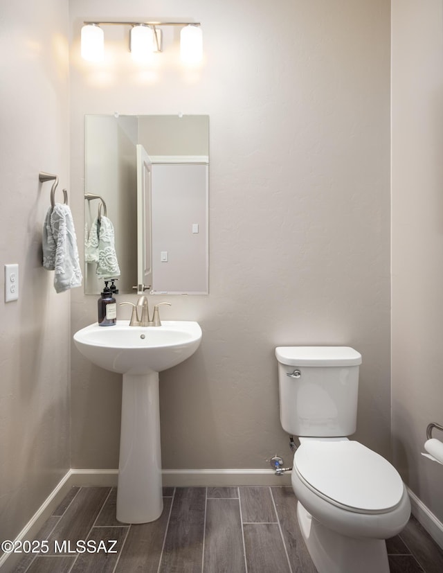bathroom with toilet, wood finish floors, and baseboards