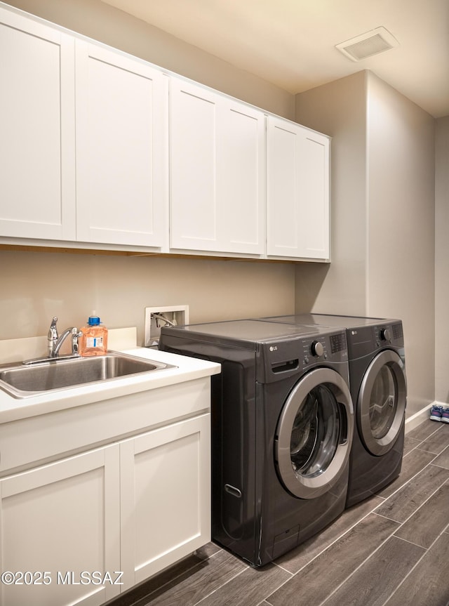 laundry room featuring visible vents, wood tiled floor, a sink, cabinet space, and independent washer and dryer