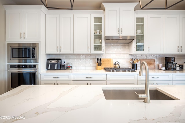 kitchen with light stone countertops, appliances with stainless steel finishes, a sink, white cabinetry, and tasteful backsplash