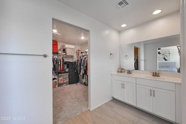 ensuite bathroom featuring a walk in closet, visible vents, a sink, and double vanity