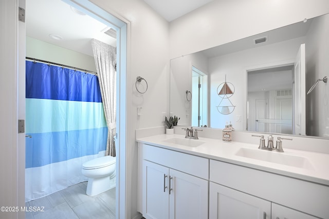 full bathroom with toilet, a sink, visible vents, and double vanity